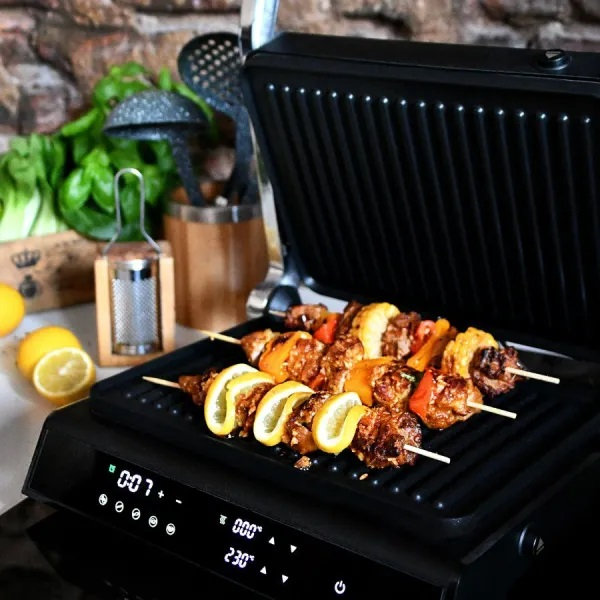 Grill z szaszłykami z mięsa i warzyw, plasterkami cytryny. W tle zioła i ceglany mur.