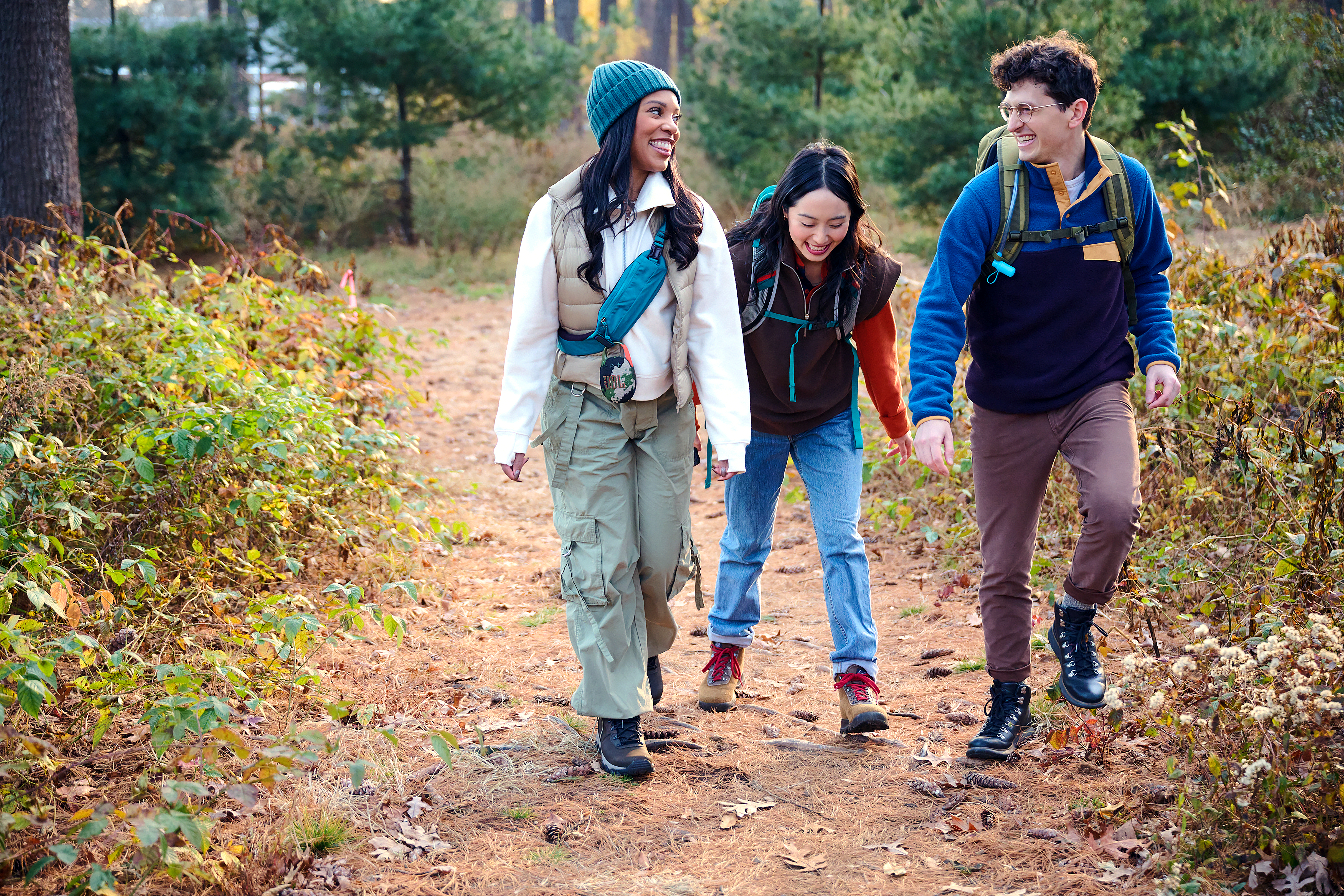 Drei Personen wandern auf einem Weg im Wald. Sie lächeln und gehen zur Kamera.