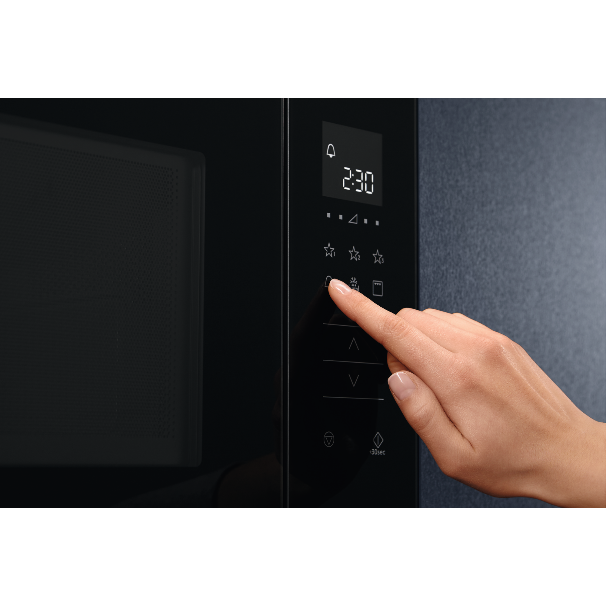 Una mano presiona un botón en un microondas. La pantalla muestra 2:30. Microondas negro en un entorno oscuro.