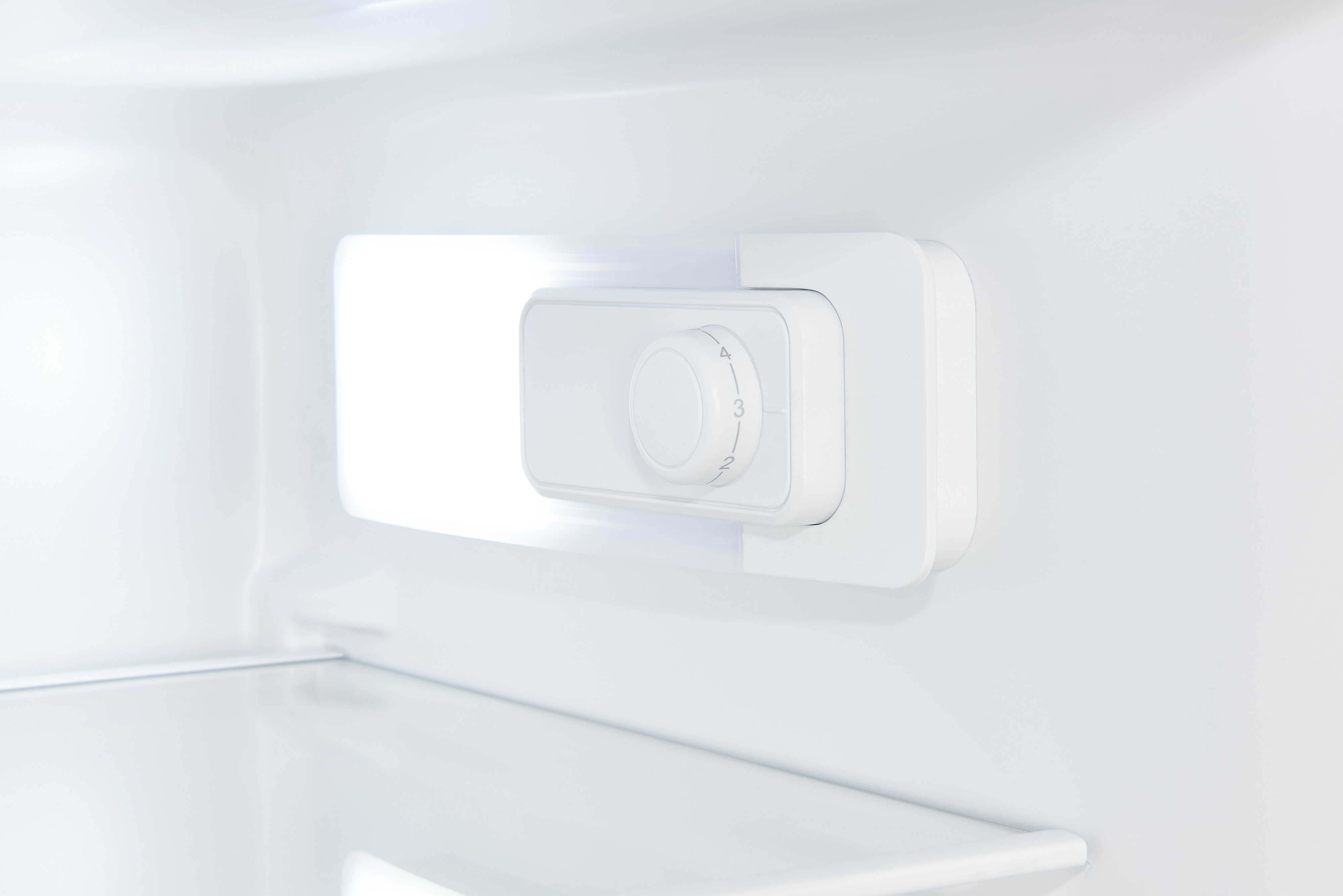 Vue intérieure d'un réfrigérateur blanc avec une commande de thermostat blanche sur le côté droit du mur.