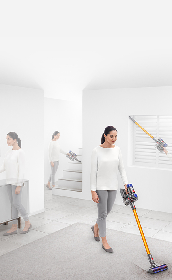 Una mujer aspira el suelo con una aspiradora Dyson amarilla y azul. Habitación blanca.