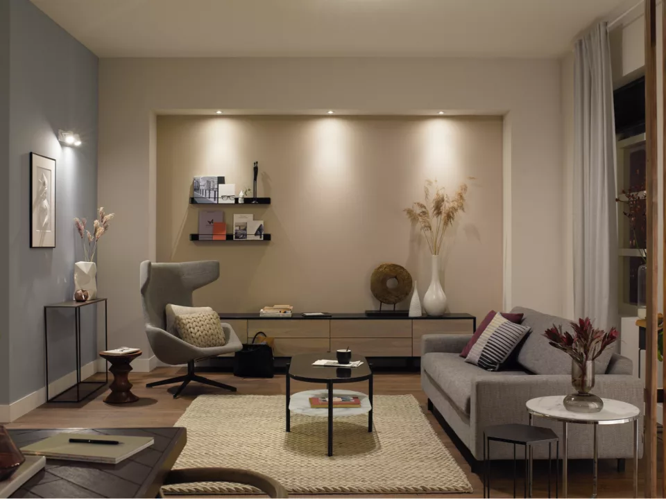 Przytulny salon w neutralnych kolorach, z sofą, dziełami sztuki i stolikiem kawowym. Lampa jest włączona.