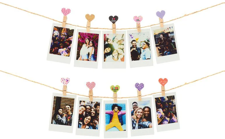Polaroid-Fotos hängen an Schnüren mit herzförmigen Clips. Fotos zeigen Gruppen von Menschen und Einzelpersonen.