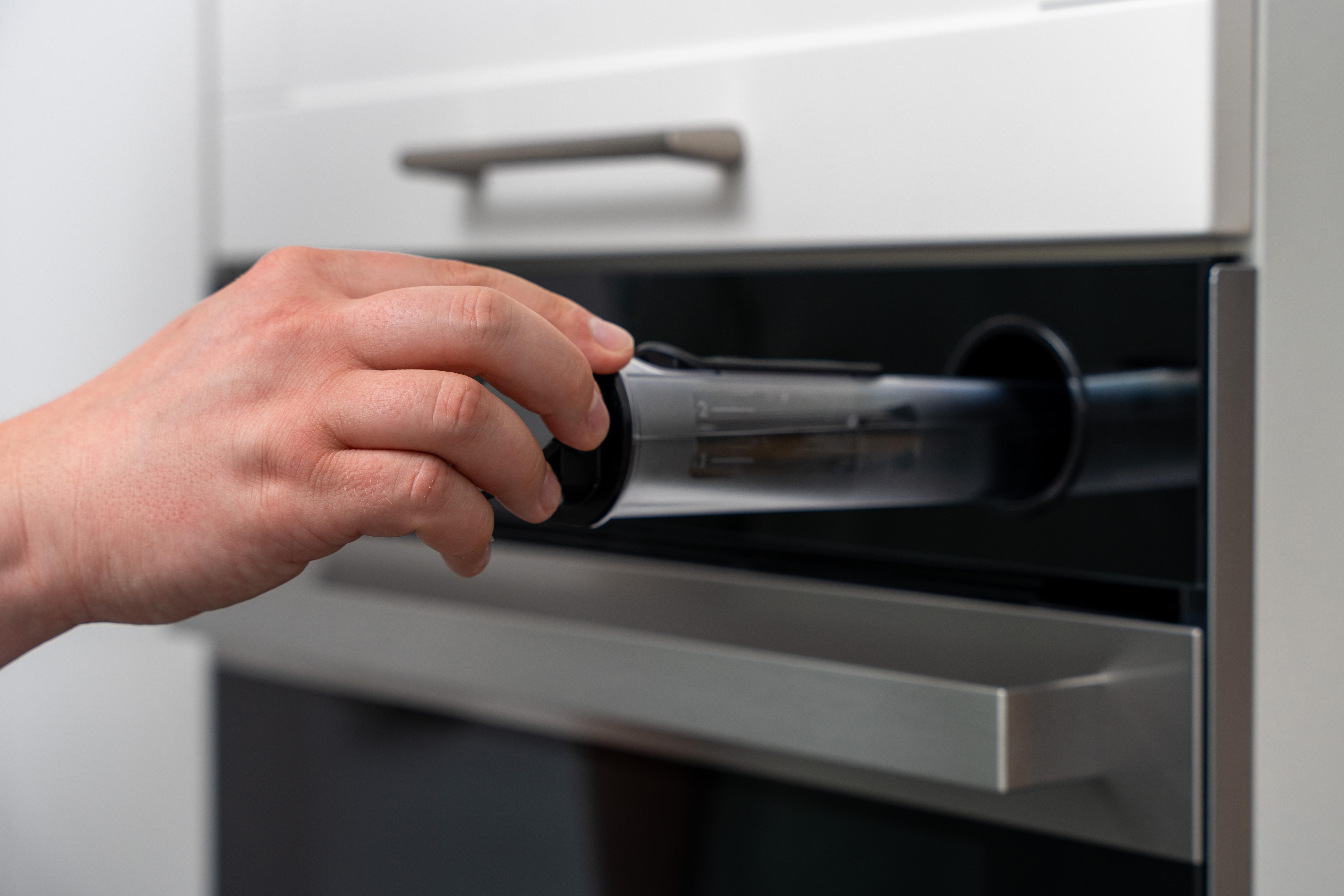 Hand, die ein transparentes Rohr in einen Einbau-Backofen einführt.