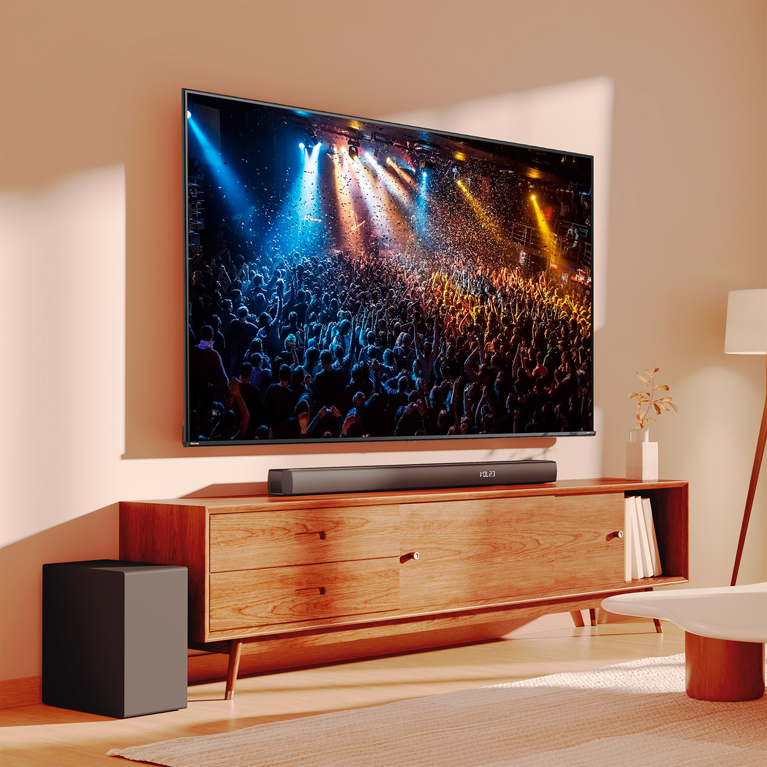 Un televisor grande muestra una escena de concierto. Está sobre un mueble de madera. Una barra de sonido está debajo. Un sub negro al lado.