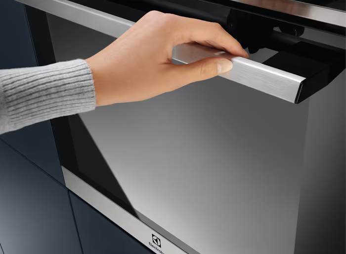 Kéz sütőajtót nyit, látható a belseje és az Electrolux márka logója.
