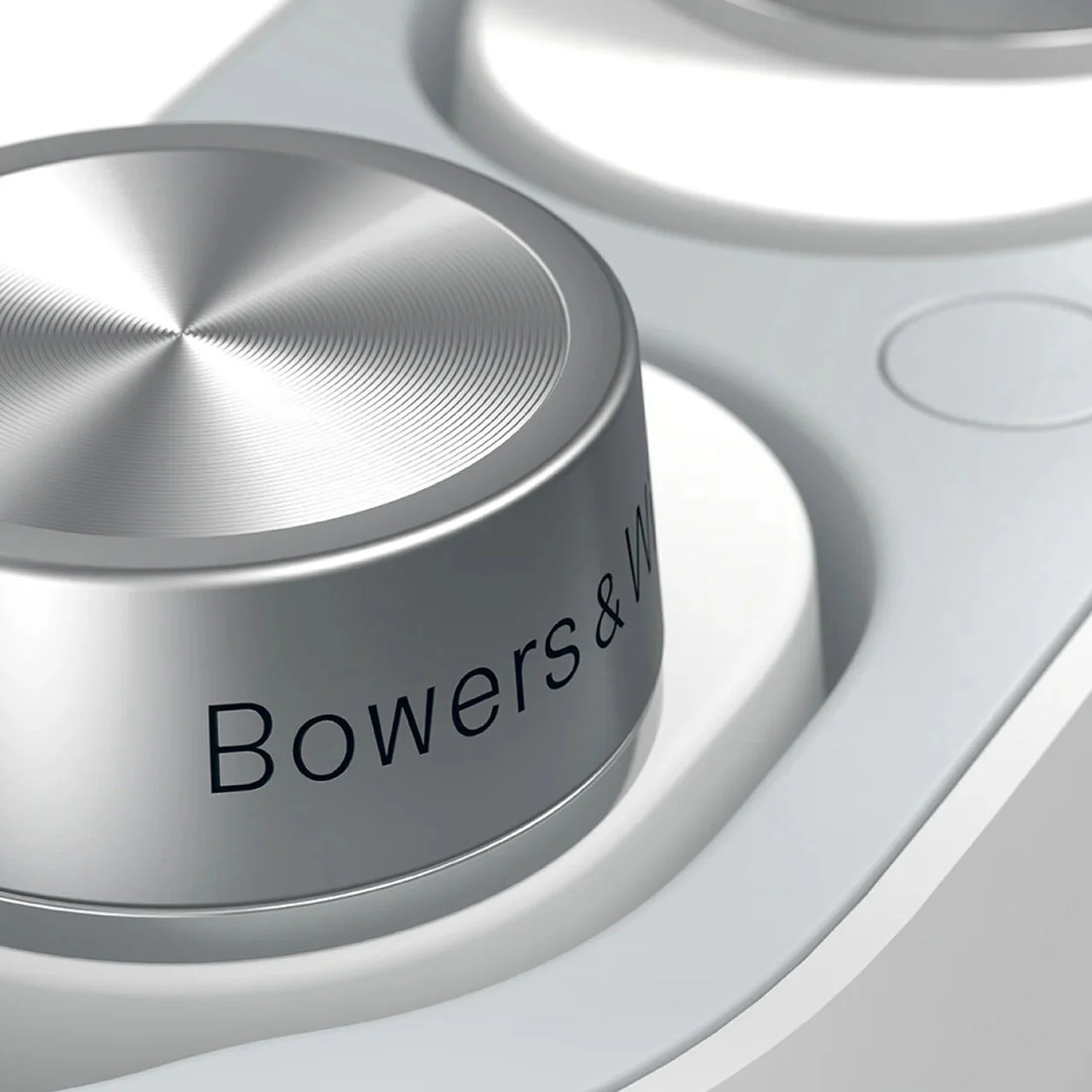 Zbliżenie srebrnego pokrętła Bowers & Wilkins na białej powierzchni.