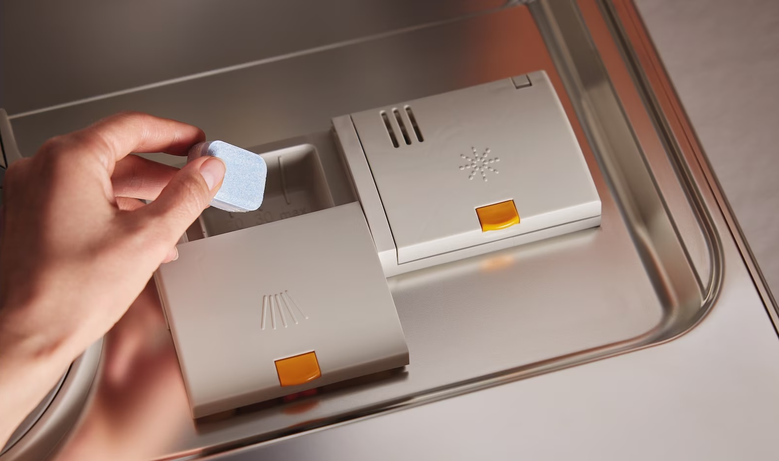 Ręka umieszcza niebieską tabletkę czyszczącą w dozowniku detergentu do zmywarki.