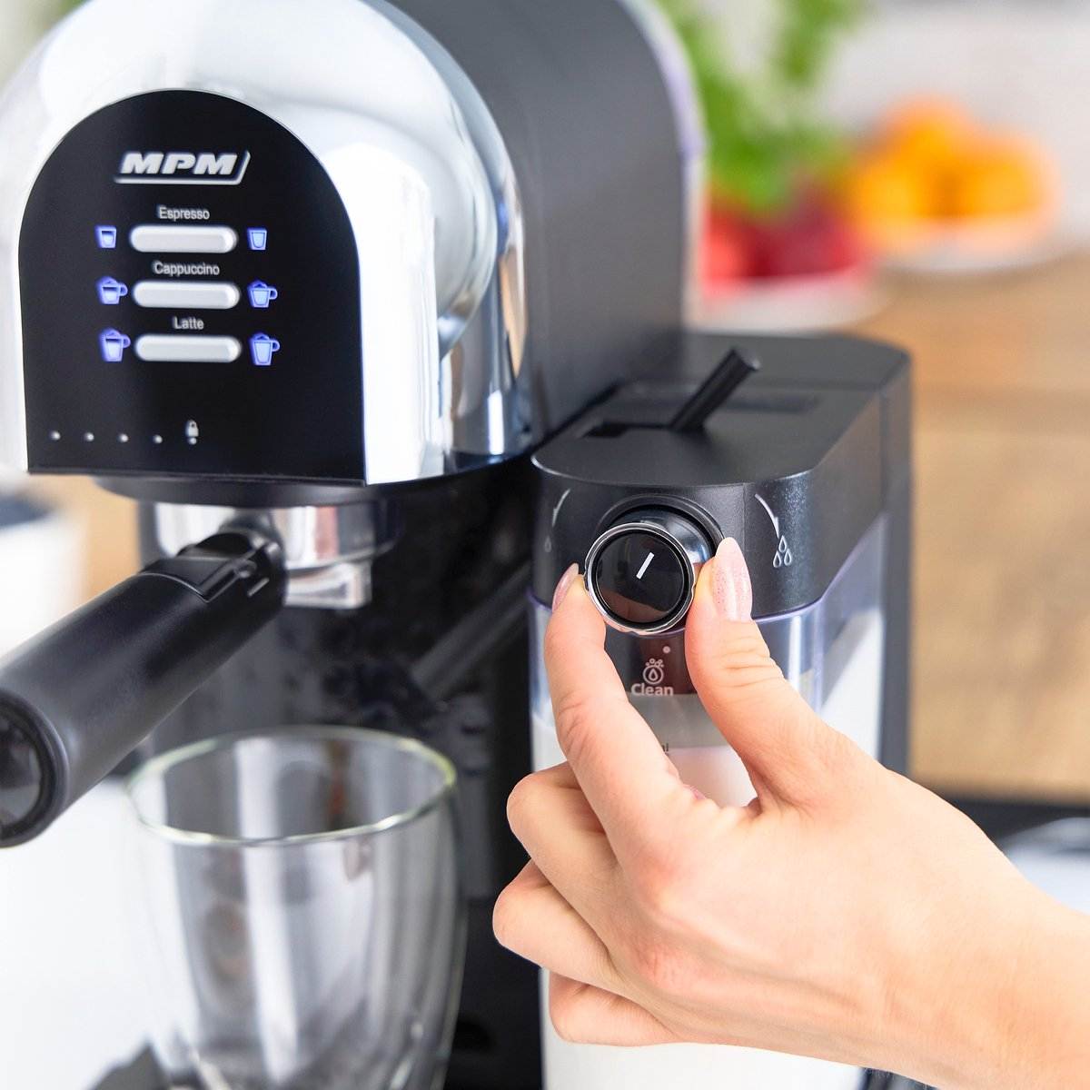 Ekspres do kawy z ręką obracającą pokrętło. Rozmyte tło z owocami.