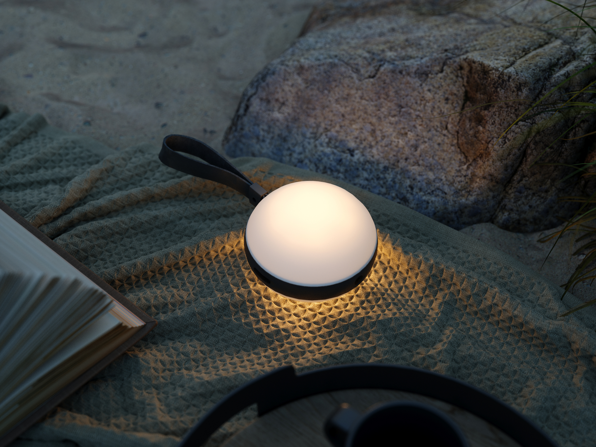 Eine leuchtende Außenlampe mit Griff, die auf einer Decke neben einem Stein und einem Buch liegt.