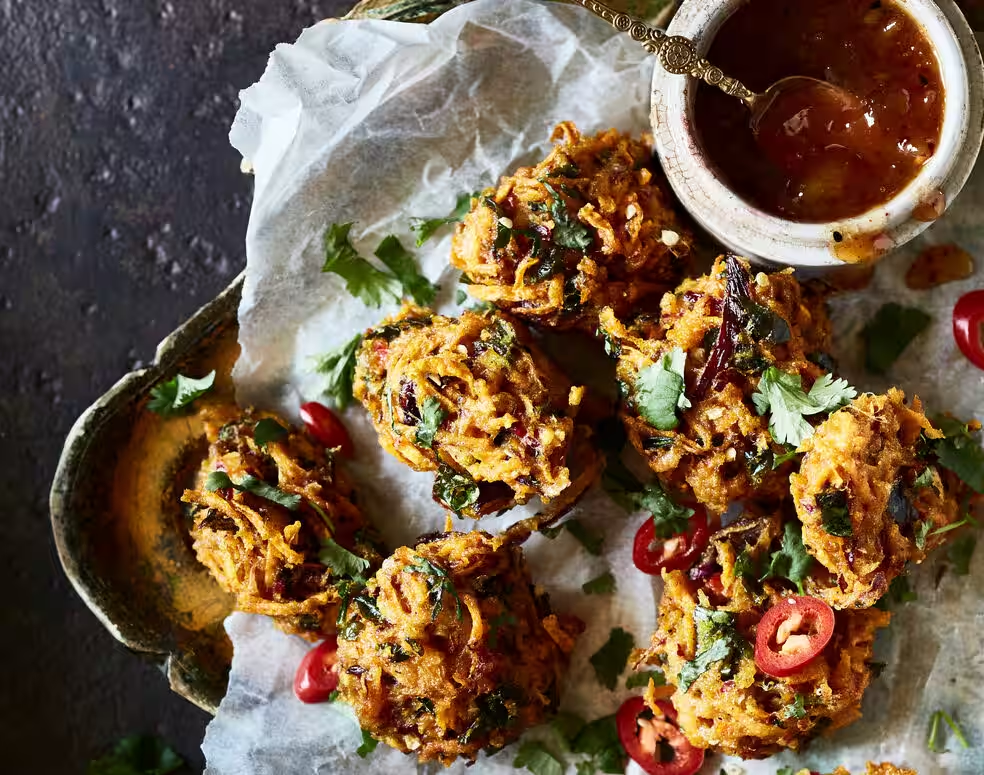 Draufsicht auf indische Pakoras mit Chutney in einer Schüssel. Das Essen befindet sich auf einer strukturierten Oberfläche.
