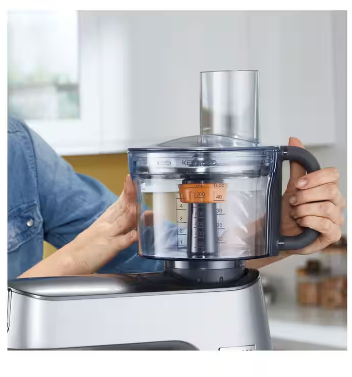 Die Hände einer Frau bedienen eine Küchenmaschine in einer Küche. Die Maschine ist silberfarben.