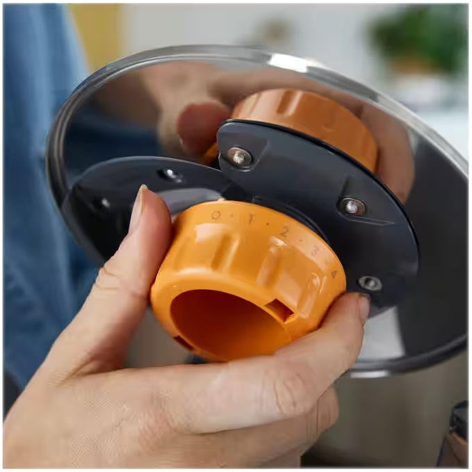 Hände, die orangefarbene Drehregler an einem Küchengerät einstellen, Teil eines Kochvorgangs.