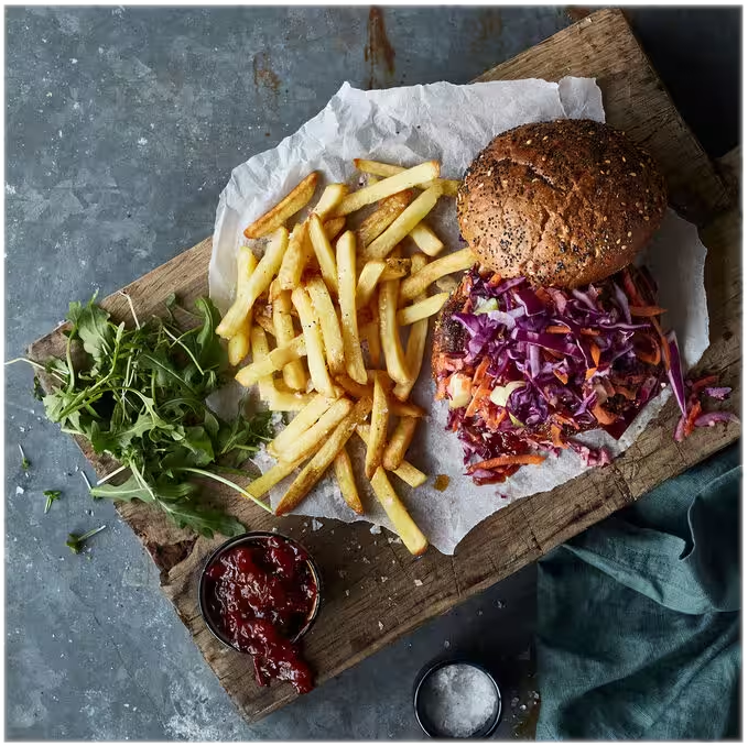 Ein Holzbrett mit Burger, Pommes, Krautsalat, Garnierung und einer kleinen Schale Soße.