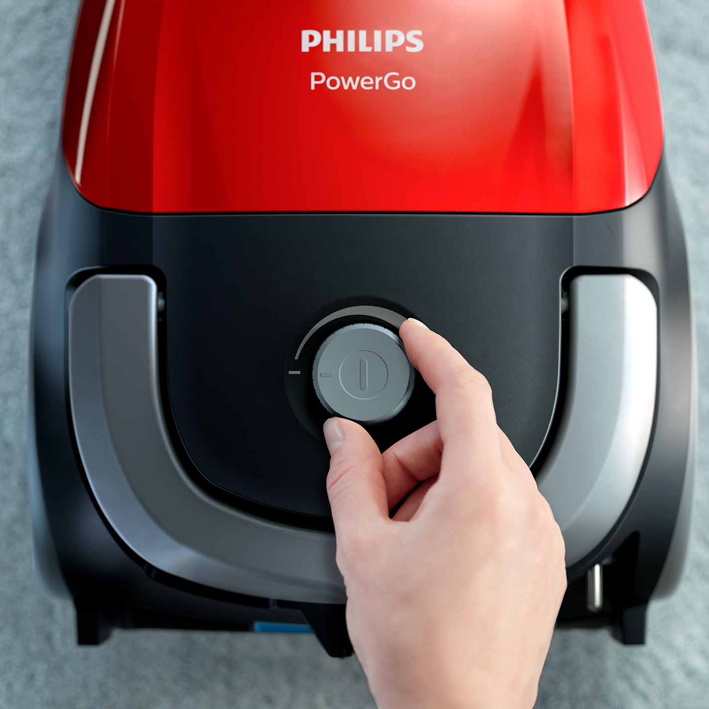 Egy kéz a beállítja a teljesítmény szabályzót egy piros-fekete Philips porszívón.