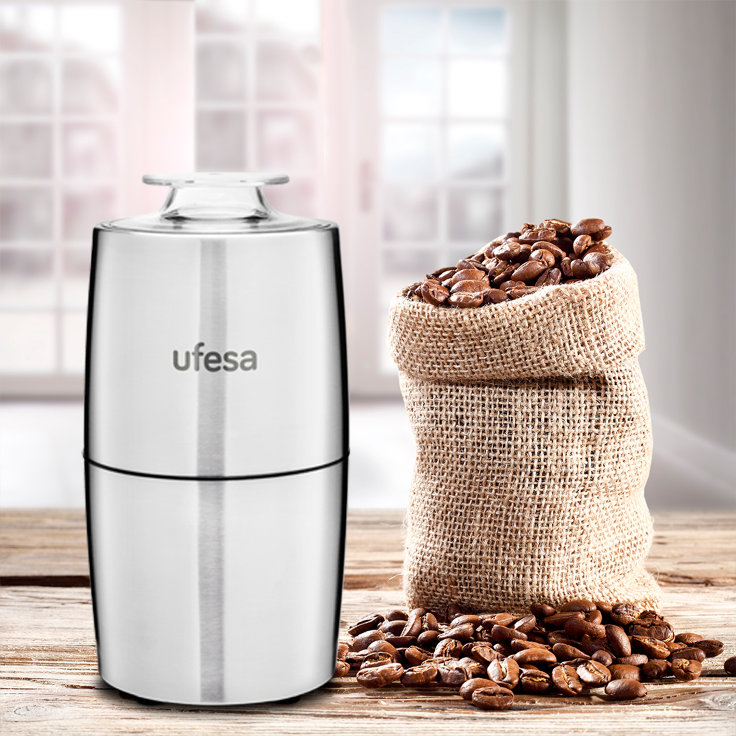 Un molinillo de café y una bolsa de arpillera llena de granos de café sobre una mesa de madera.