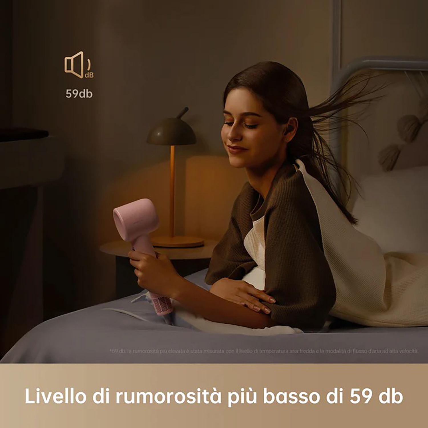 Una donna sdraiata sul letto, tiene un asciugacapelli rosa vicino al viso, con il testo "59db".