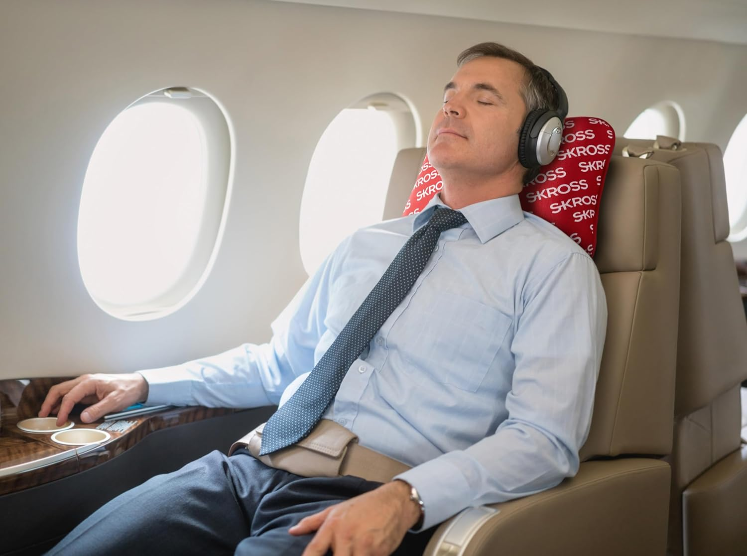 Mann schläft im Flugzeug mit Kopfhörern. Er trägt Krawatte und Anzug.