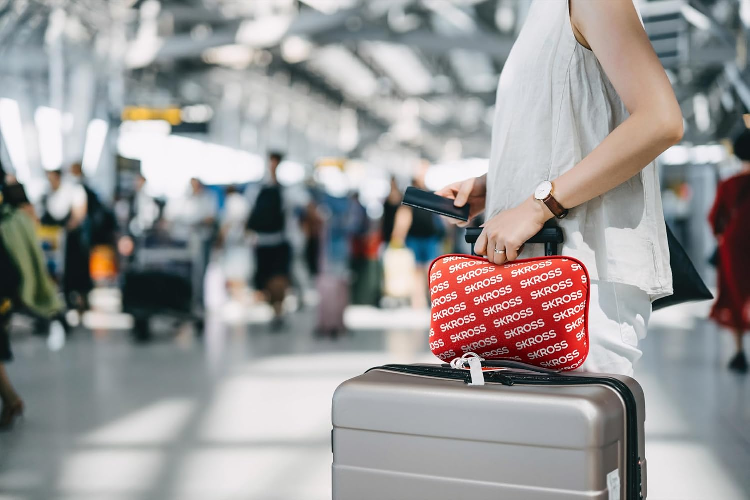 Frau mit Gepäck am Flughafen. Sie hält eine rote Tasche und einen Koffer.