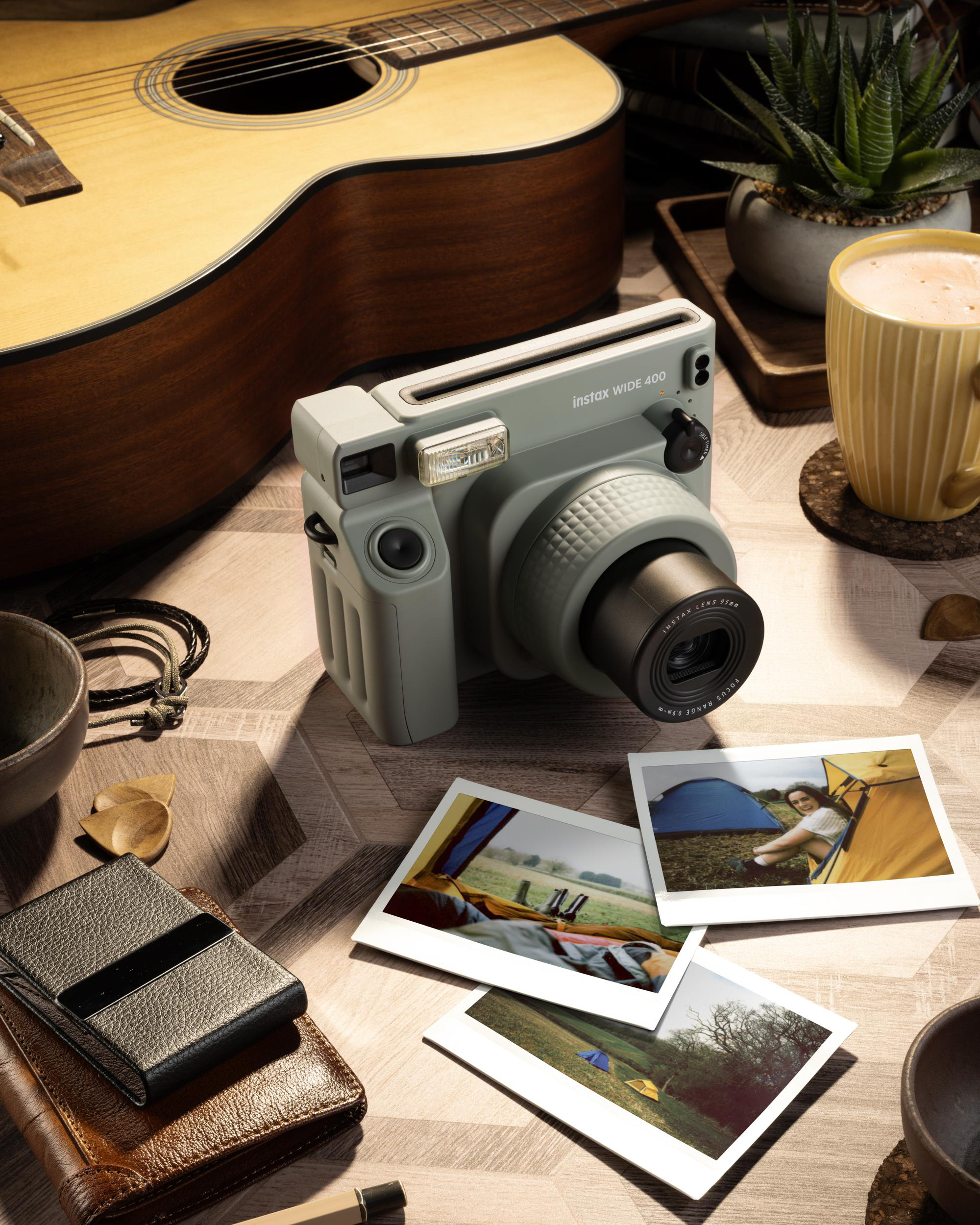 Eine Kamera, Fotos, Gitarre und Kaffeetasse auf einem Holztisch, mit verschiedenen Objekten.