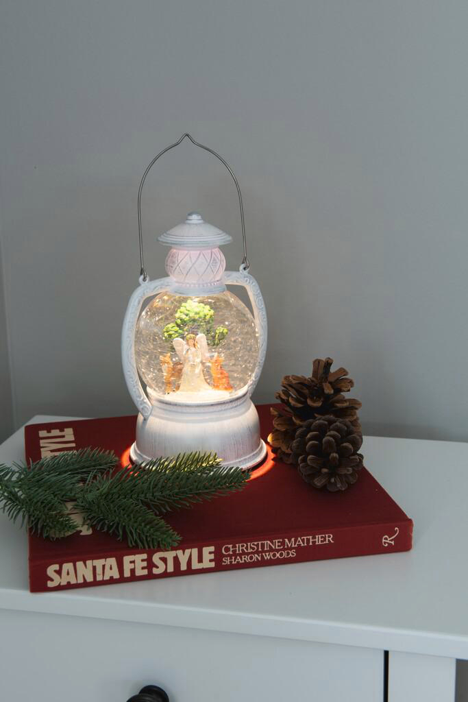 Schneekugel mit einer weißen Laterne, einem Engel, Tannenzapfen und einem Buch mit Santa Fe Style.