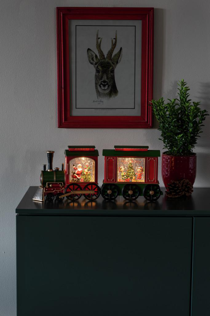 Ein dekorierter Weihnachtszug mit Lichtern auf einem dunkelgrünen Schrank.
