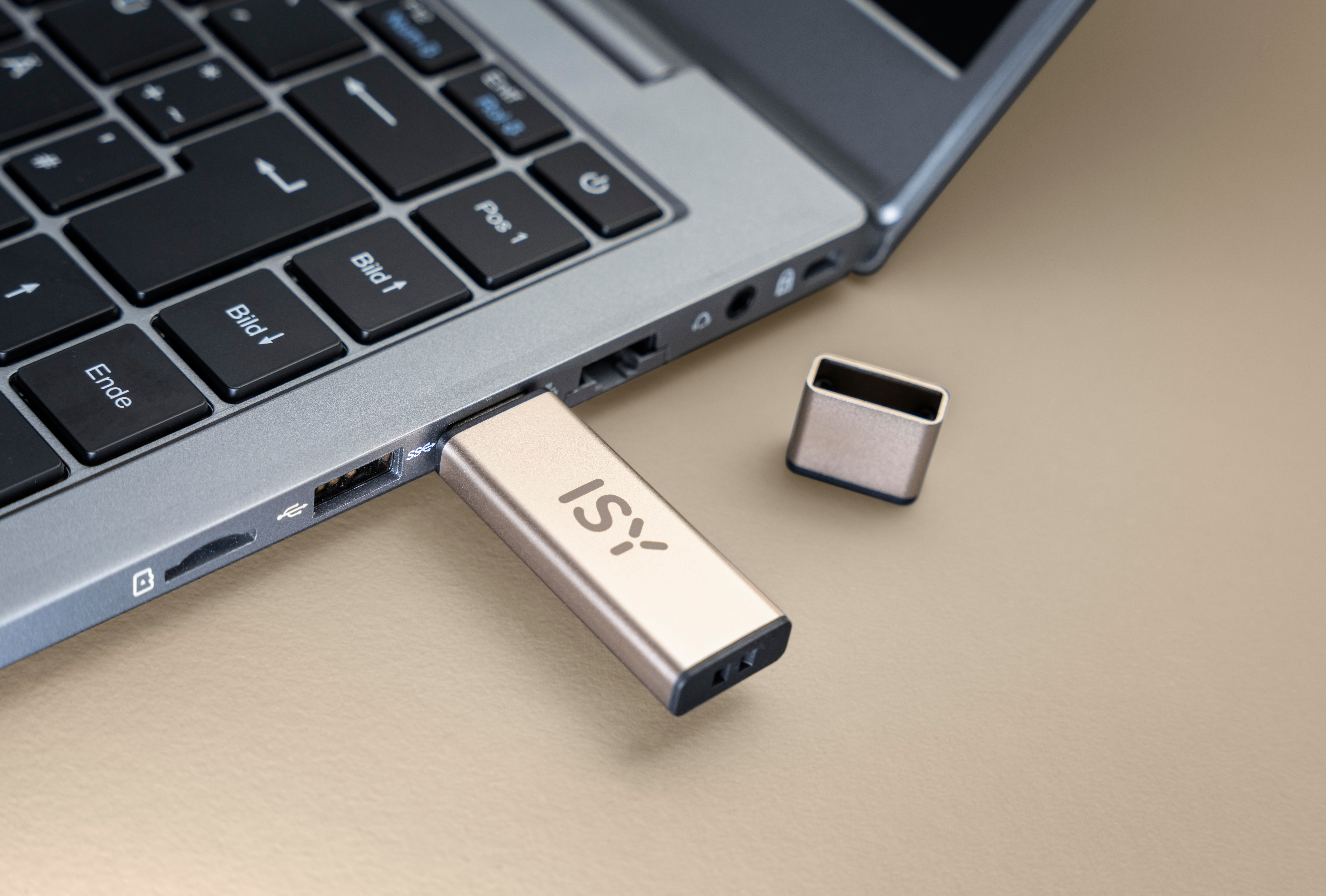 Ein goldfarbener ISY USB-Stick in einen Laptop gesteckt. Der Laptop steht auf einer hellbraunen Oberfläche.