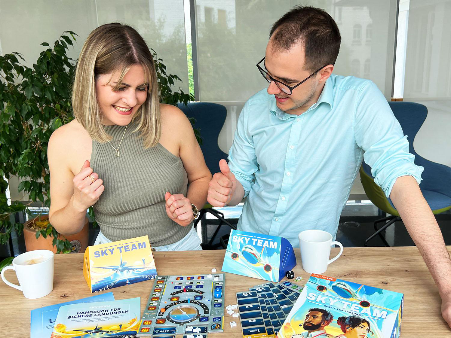 Zwei Personen lächeln über einem Brettspiel. Spielboxen und Teile liegen auf dem Tisch.