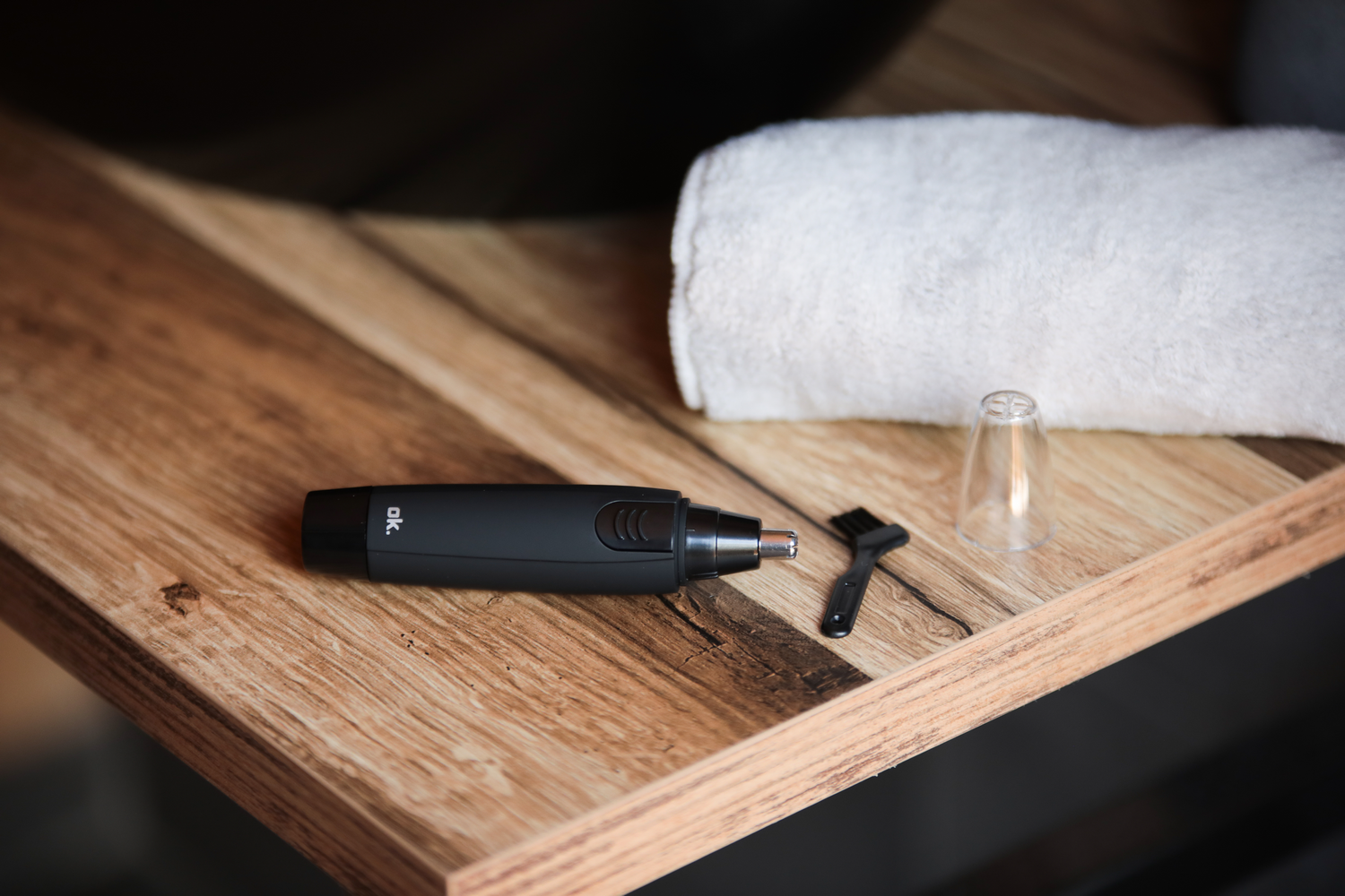 Recortador de vello nasal negro, cepillo y cubierta sobre superficie de madera con toalla blanca.
