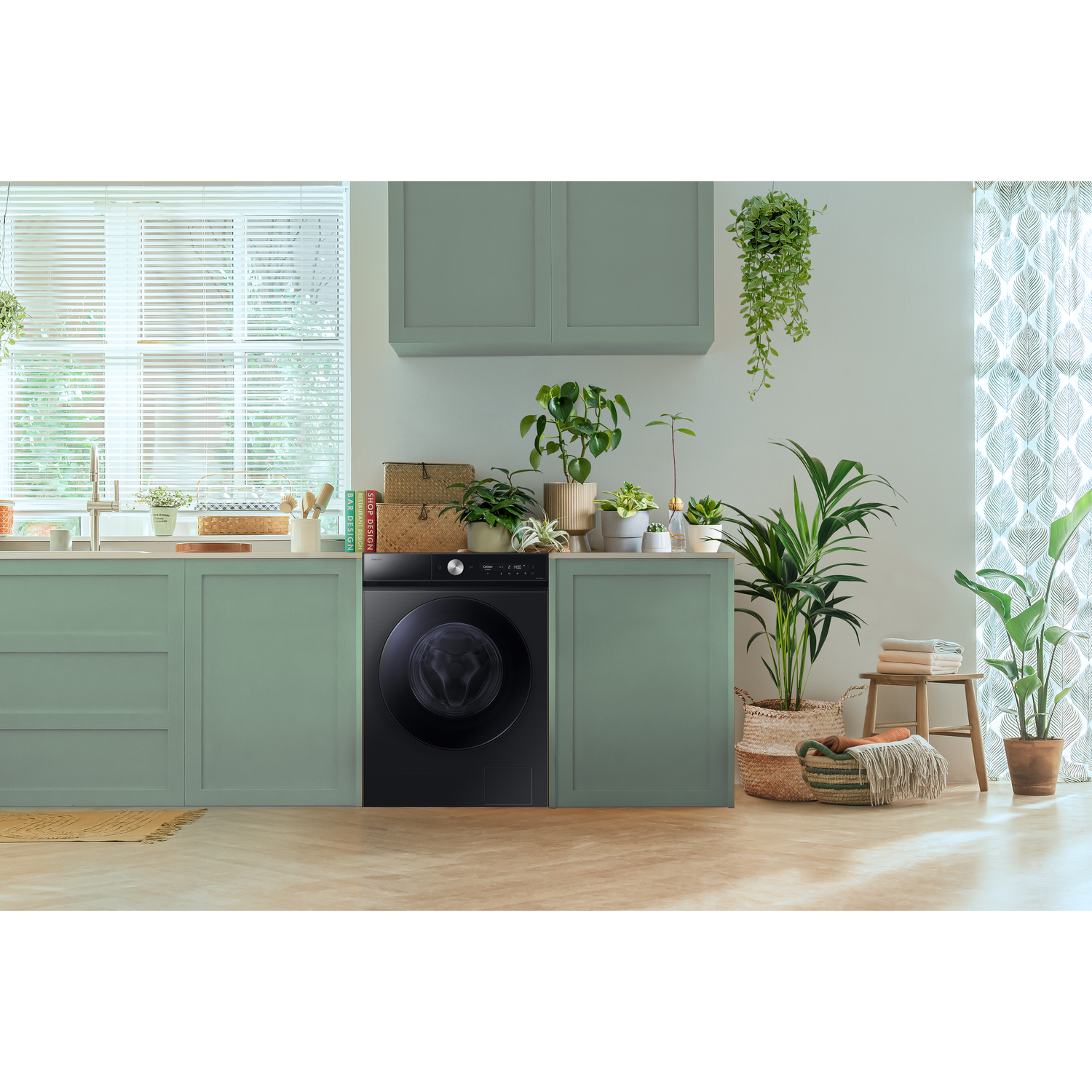 Keuken met wasmachine, planten, kasten en raam met jaloezieën.