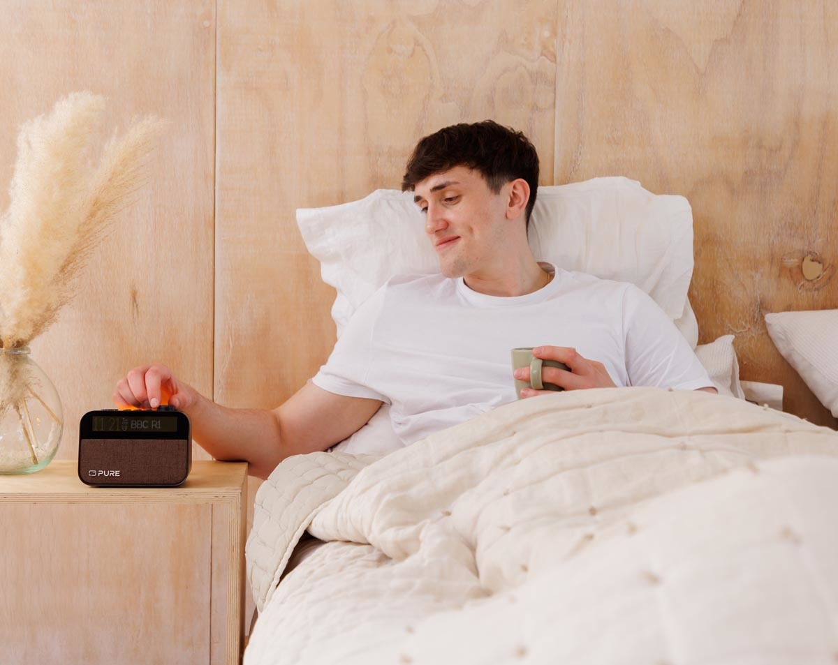 Homme au lit, allumant une radio. A côté de lui, un vase et des fleurs.