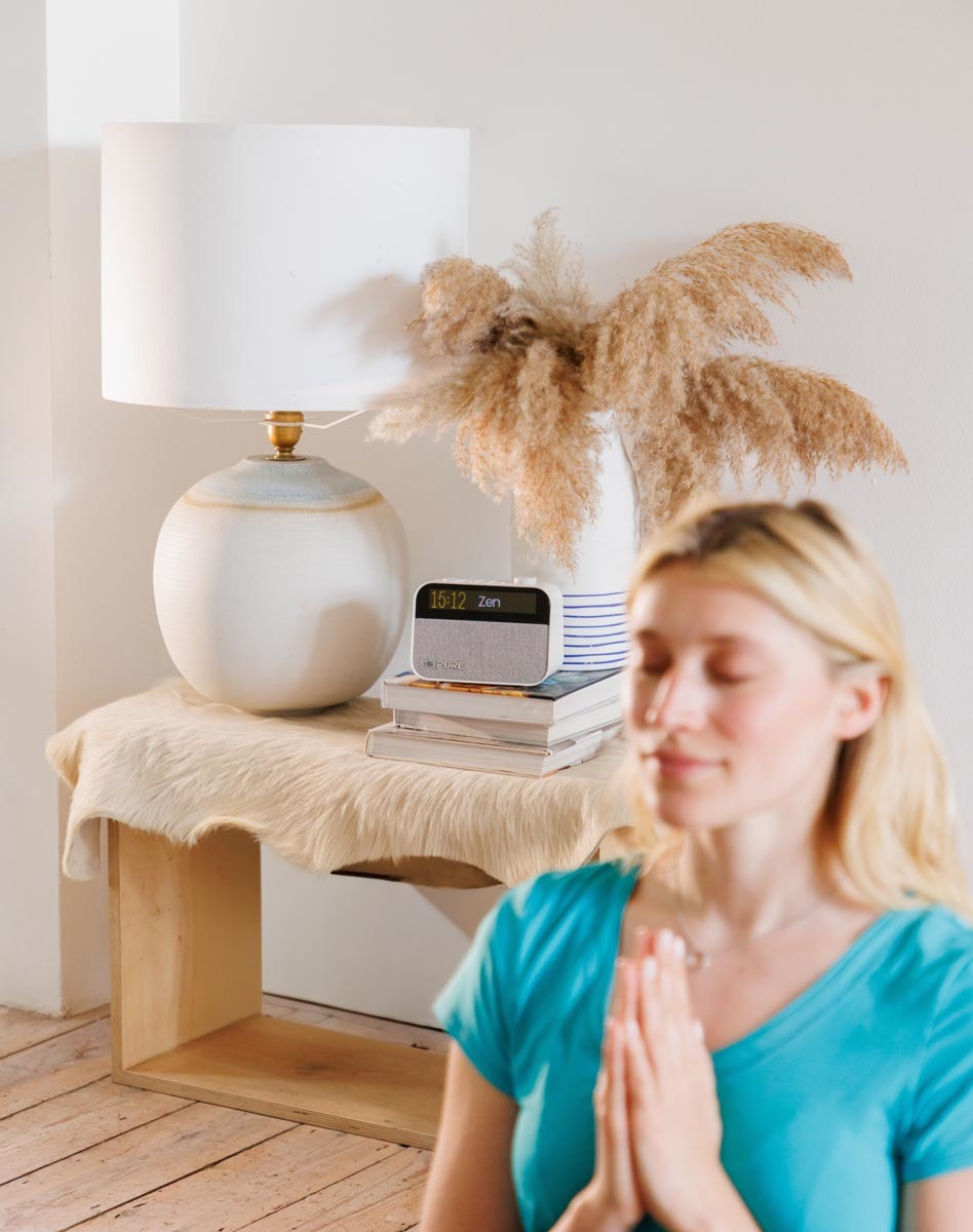 Une femme médite les mains jointes, une lampe et une radio Zen sont derrière.