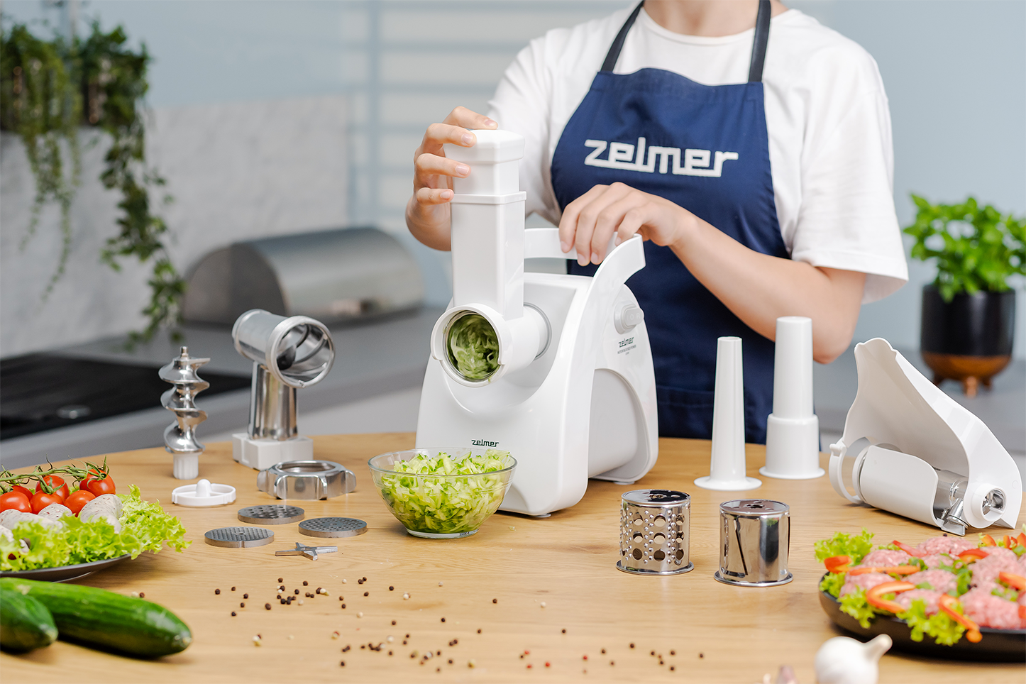 Nő fehér konyhai robotgépet használ különböző tartozékokkal és hozzávalókkal.