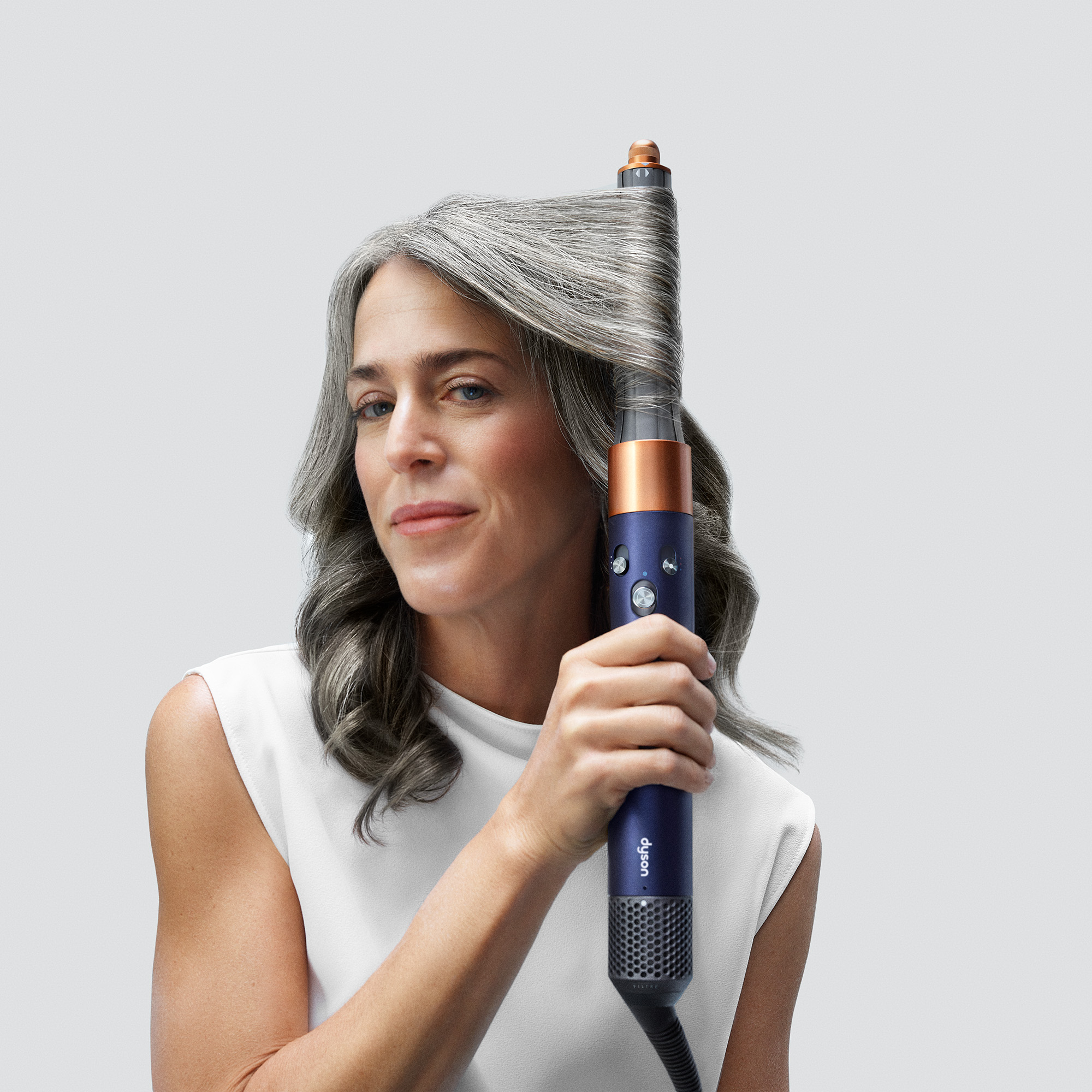 Frau mit grauem Haar, die ein blaues und kupferfarbenes Haarstyling-Tool verwendet.