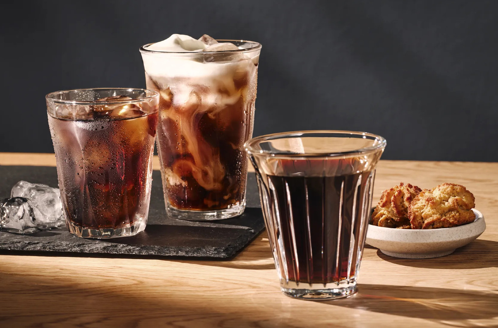 Trzy szklanki napojów kawowych z lodem i pianką oraz ciasteczka.