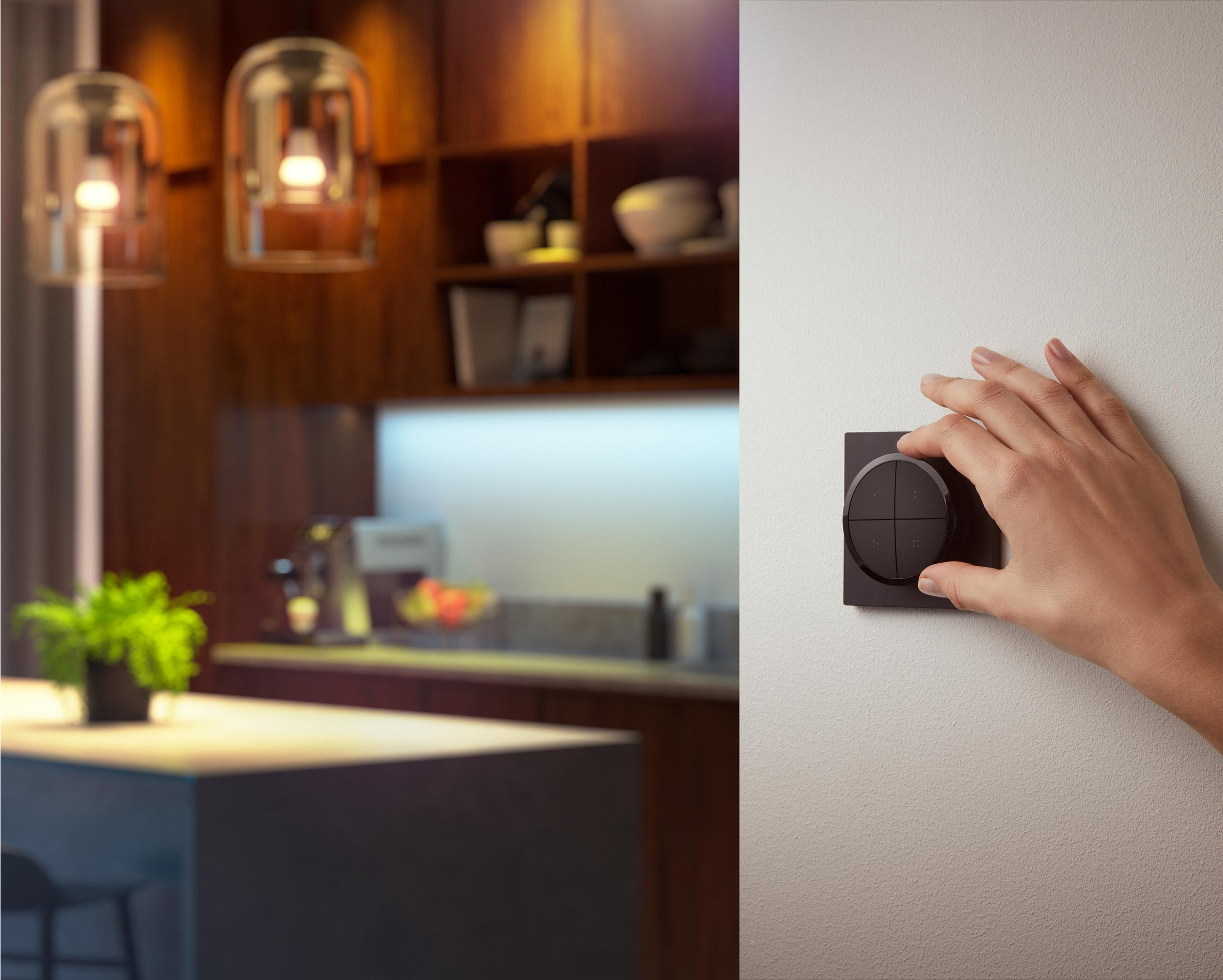 Une main tournant un bouton de commande noir sur un mur blanc à côté d'une cuisine.