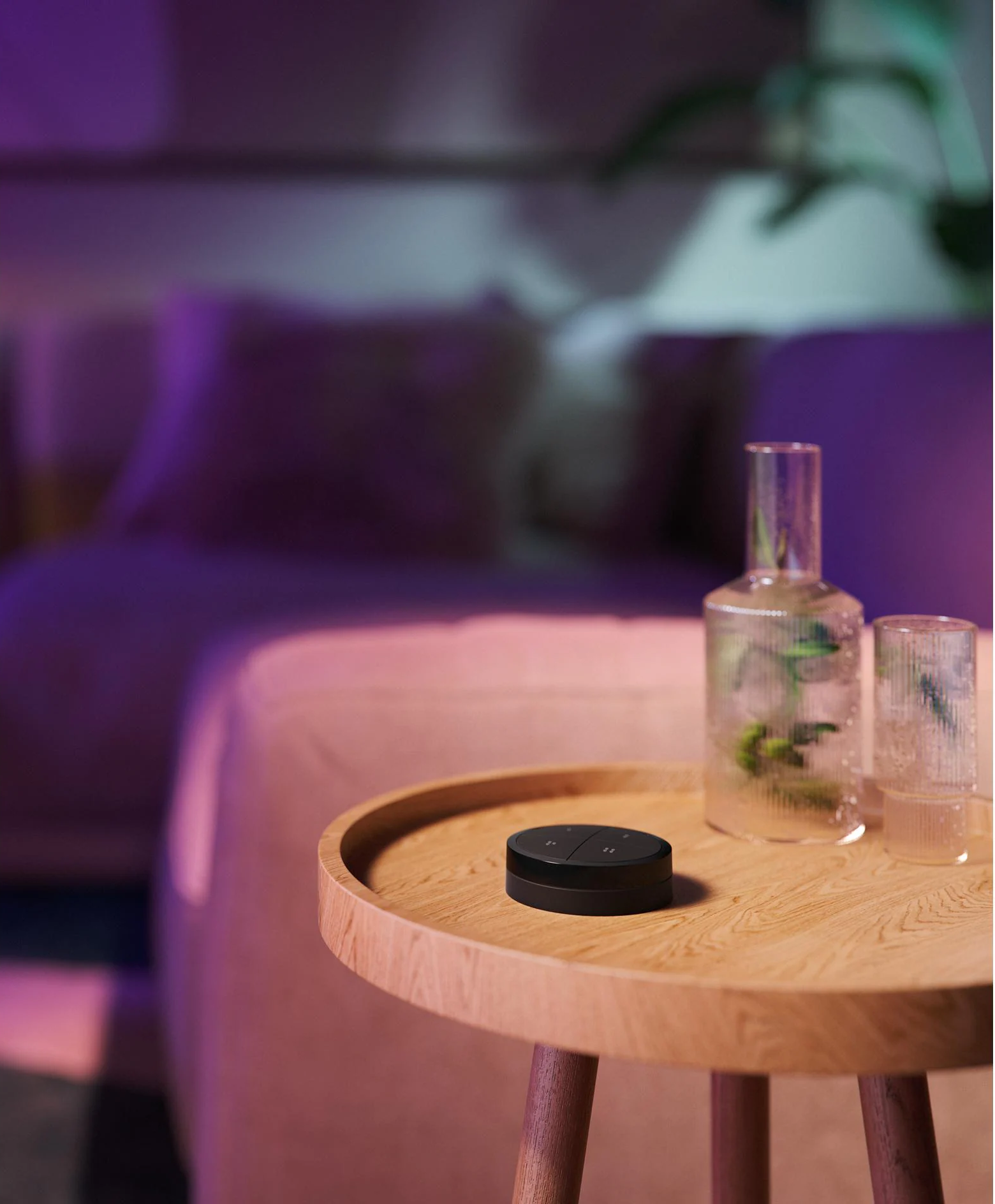 Une télécommande domotique noire sur une table en bois. Bouteille et verre à côté.