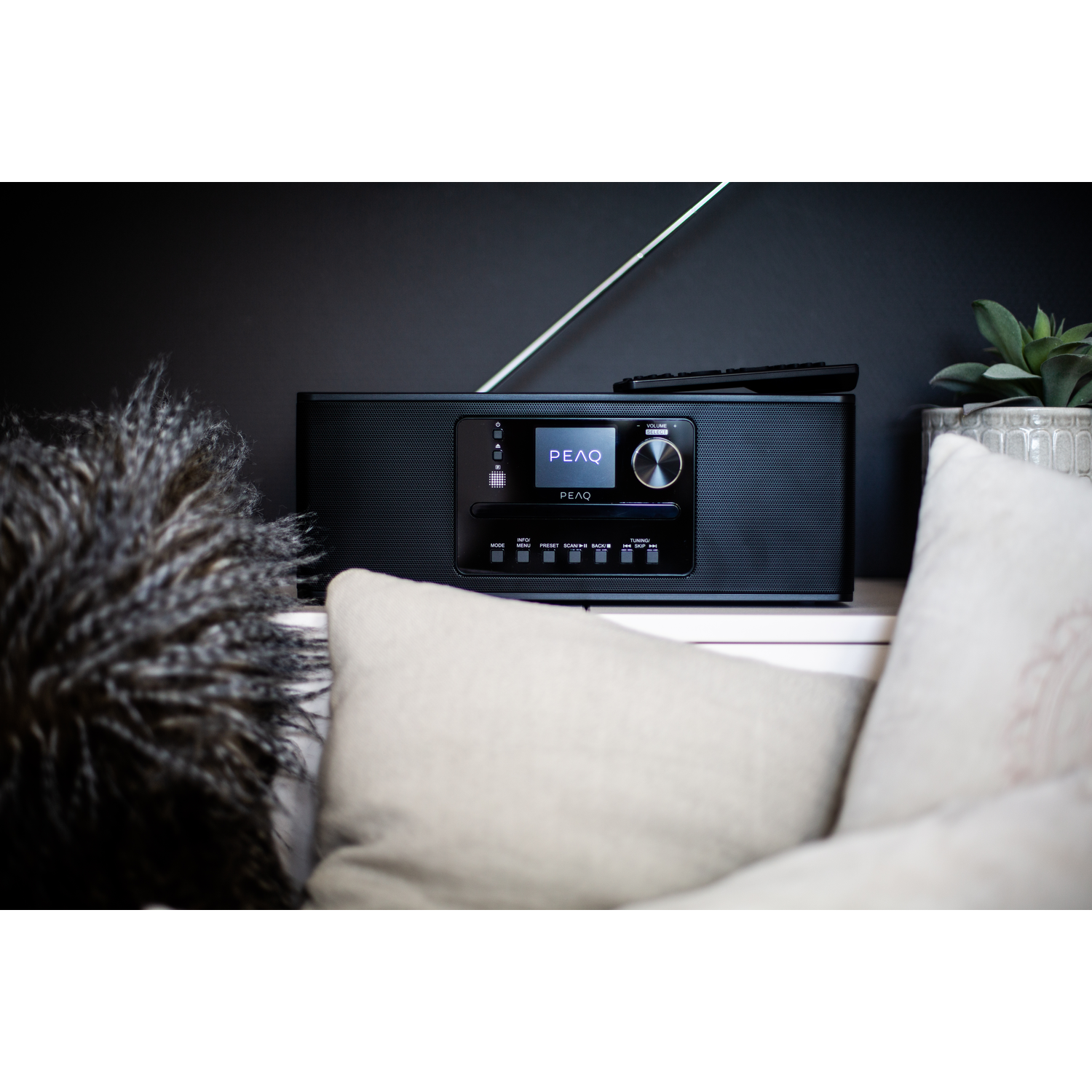 Black digital radio with a remote control on a white surface.