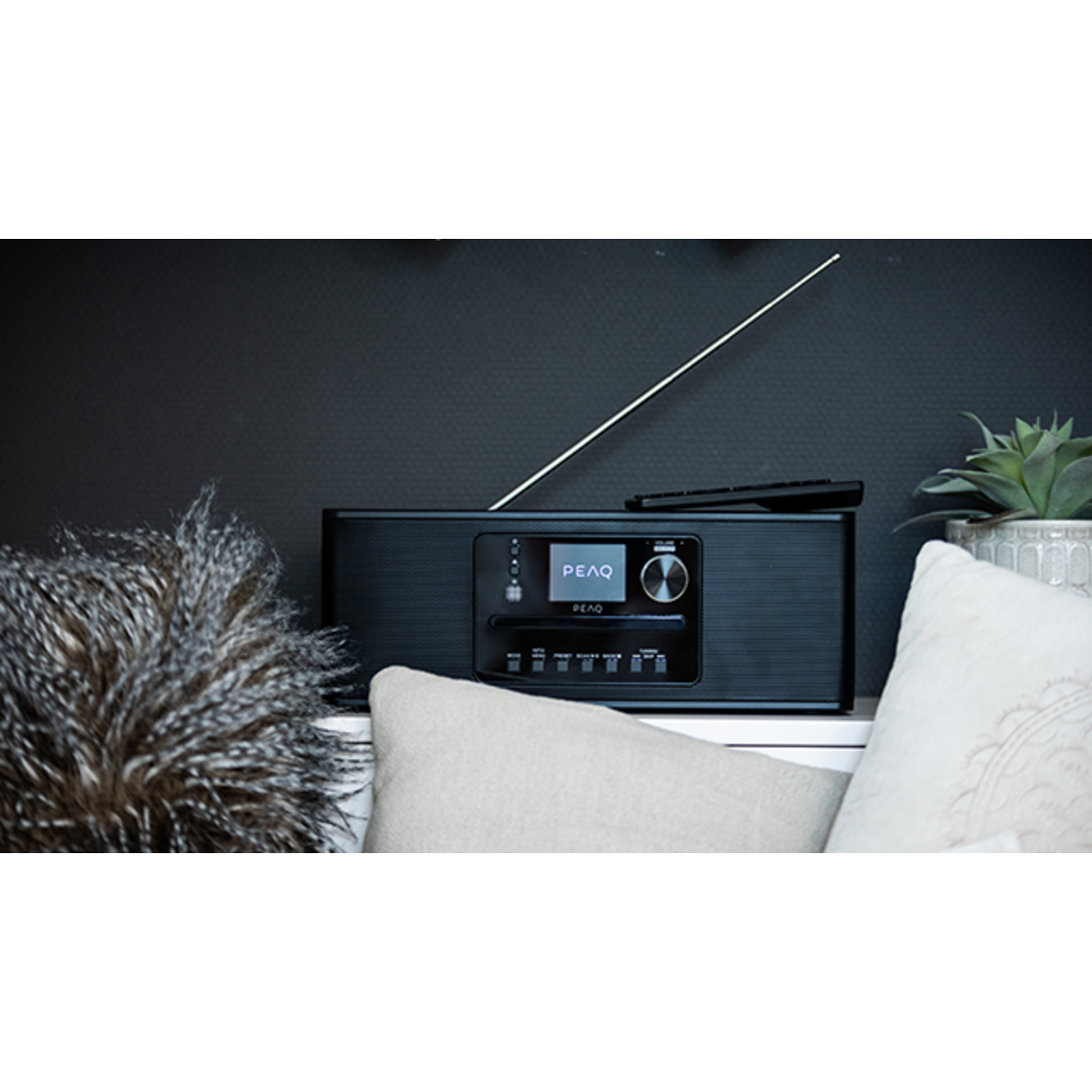 A black PEAQ radio with a display, antenna, and remote control on a surface.