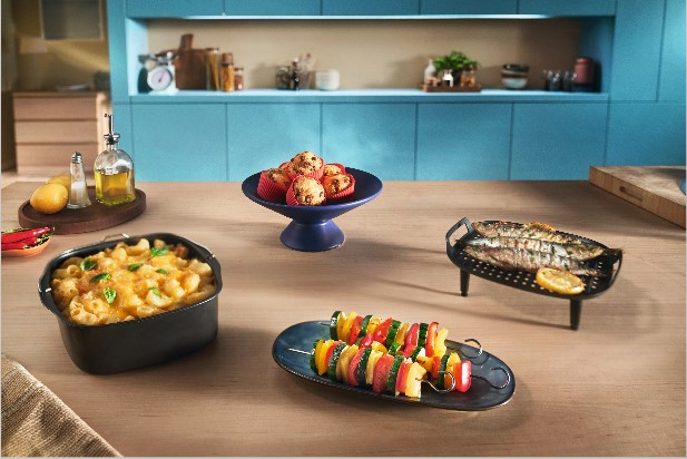 Comida en la mesa: macarrones con queso, brochetas, magdalenas, pescado, frente a una cocina.