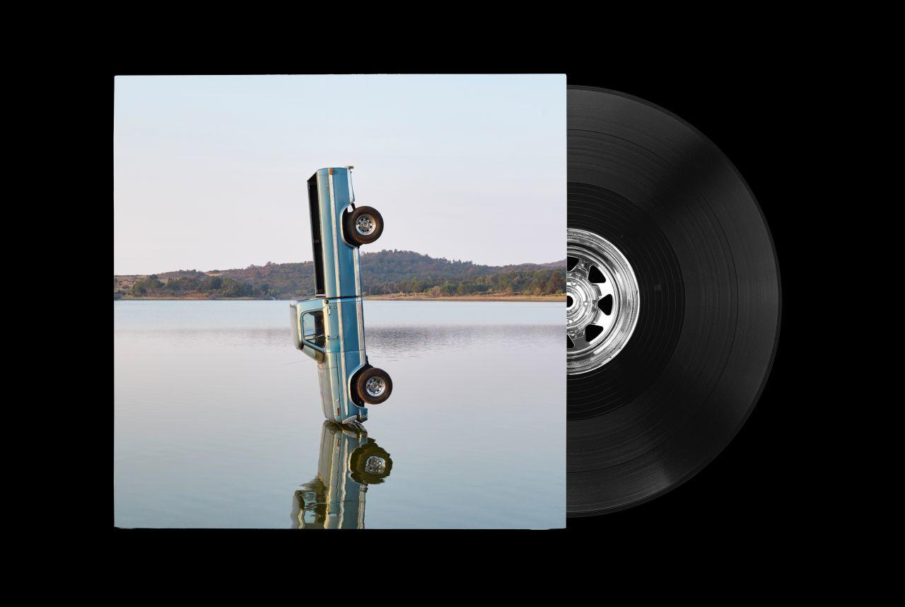 Albumcover mit umgekehrtem LKW im Wasser und Schallplatte.