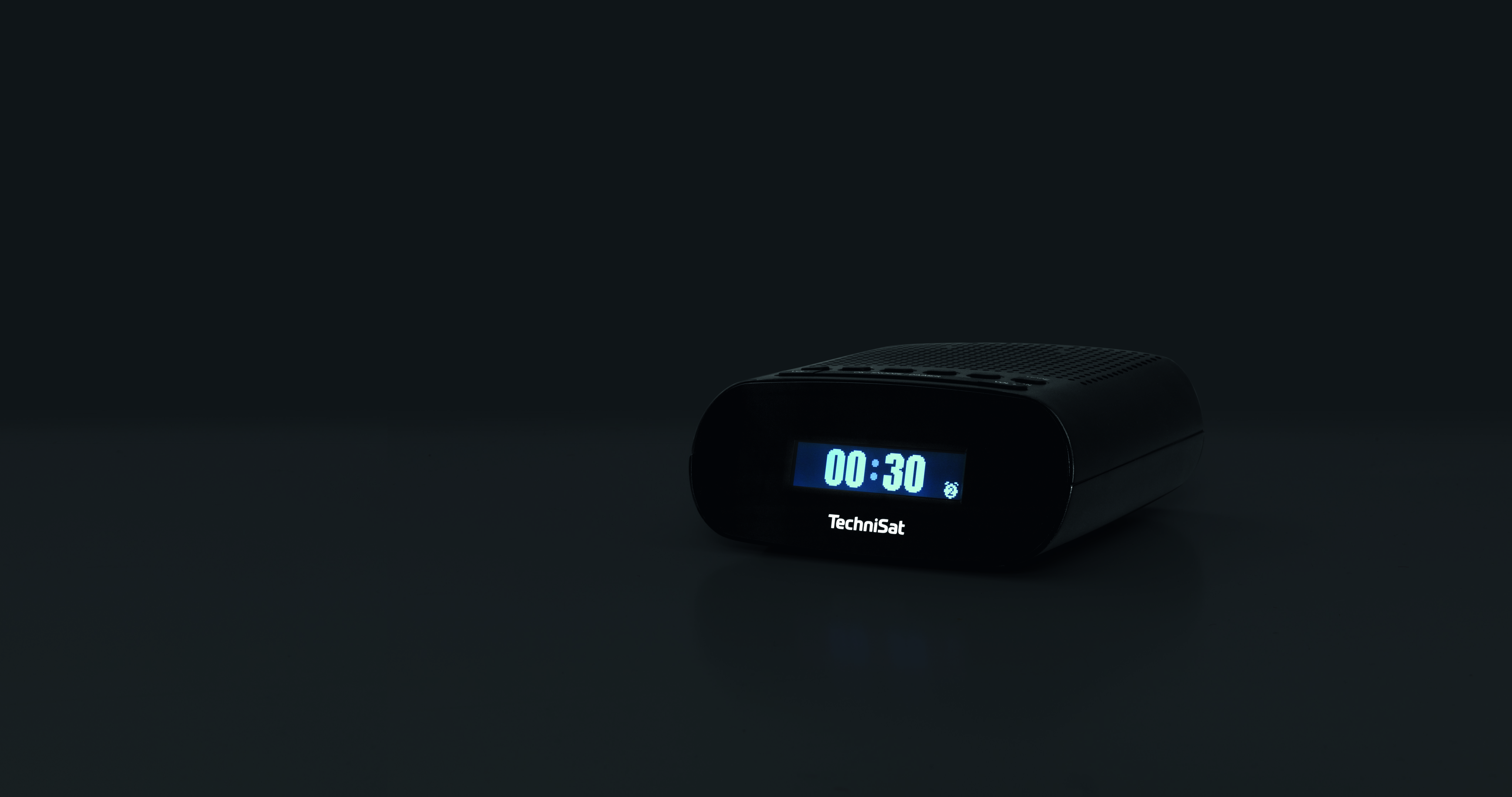 Ein schwarzer TechniSat-Wecker, der 00:30 auf einer dunklen Oberfläche anzeigt.
