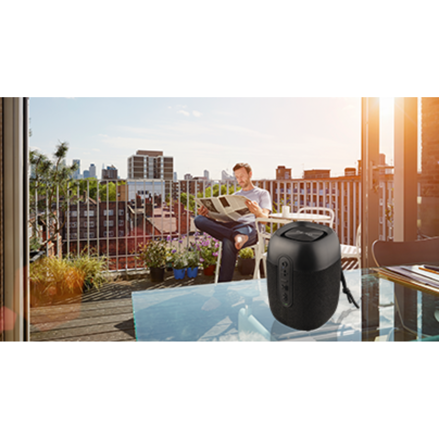 Een persoon die een krant leest op een balkon. Een draagbare luidspreker staat op een tafel in de buurt.