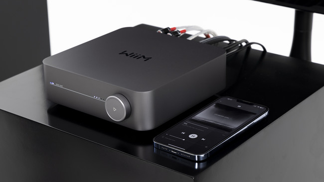 Uno streamer audio Wiim nero con un telefono che mostra un'app musicale.