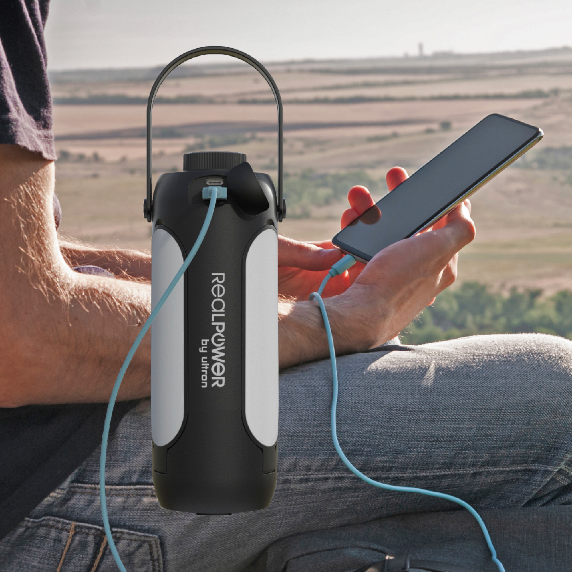 Eine Person sitzt draußen und lädt ein Telefon mit einer schwarz-weißen tragbaren Powerbank auf.