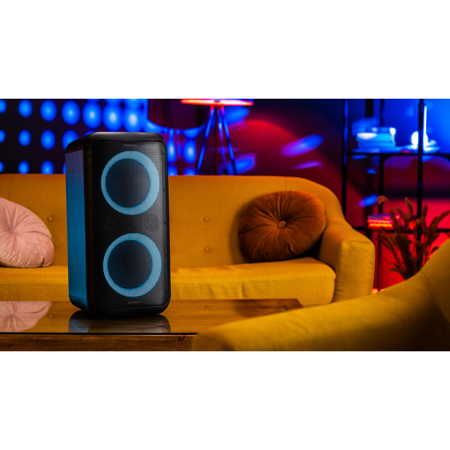 Black speaker with two light rings, set on a table in a room with a yellow sofa and blue lights.