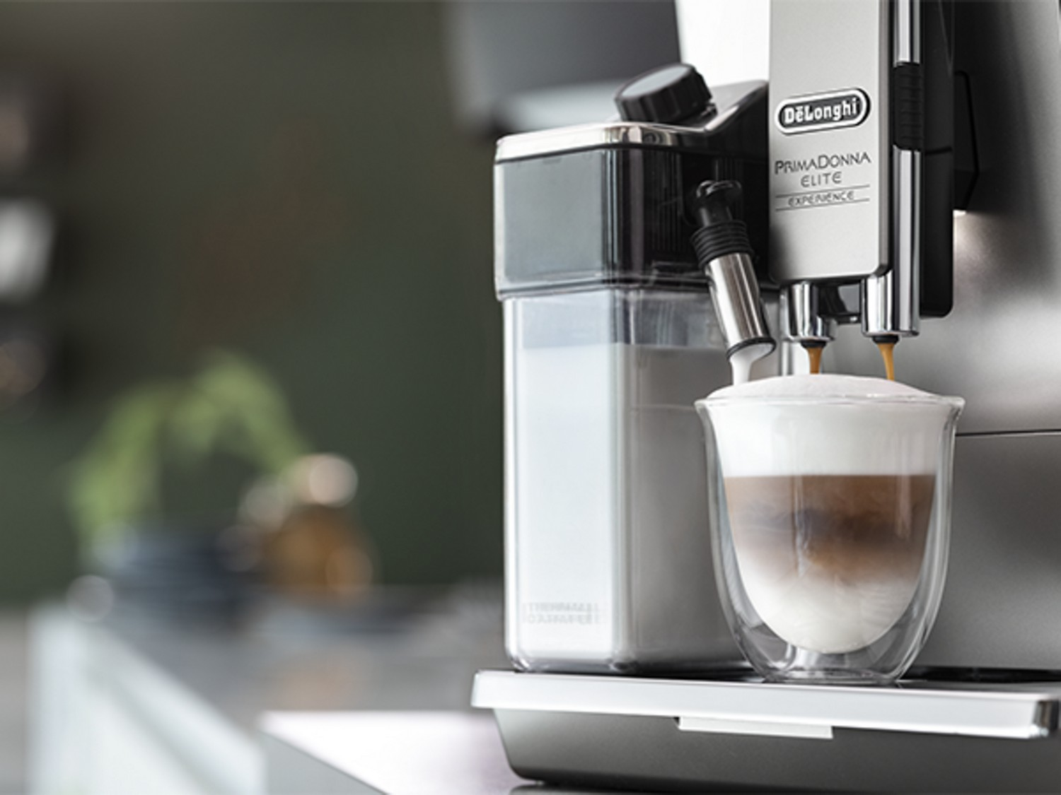 Máquina de espresso vertiendo café en un vaso con leche y espuma en capas.