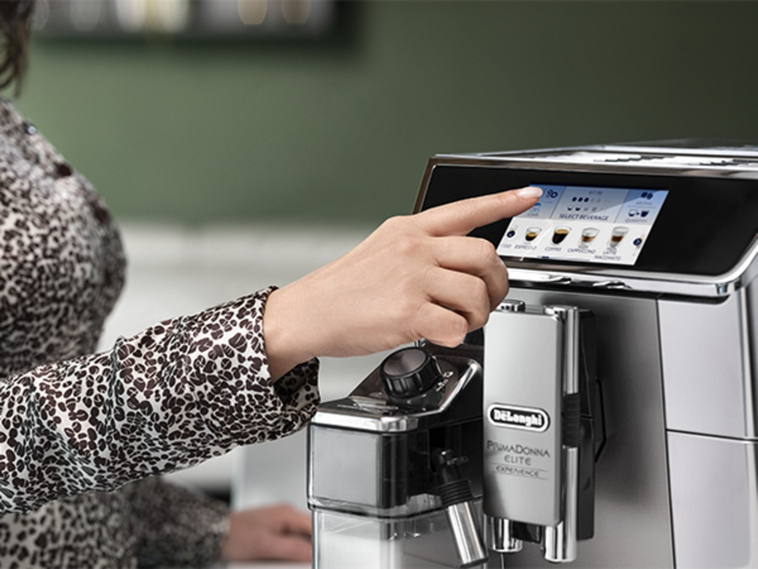 La mano de una mujer toca una pantalla táctil de cafetera, con opciones de café.
