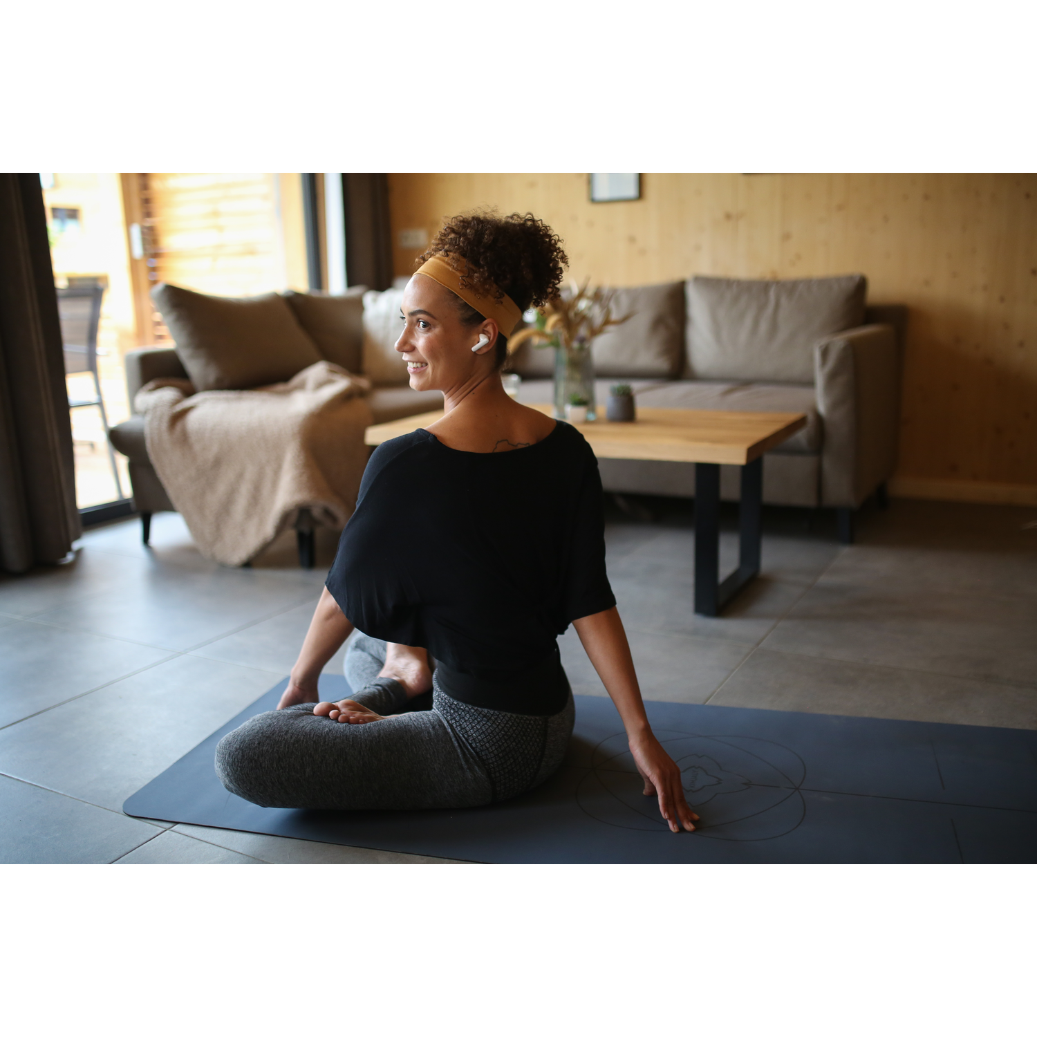Woman doing yoga on a mat. She wears a headband and earbuds.