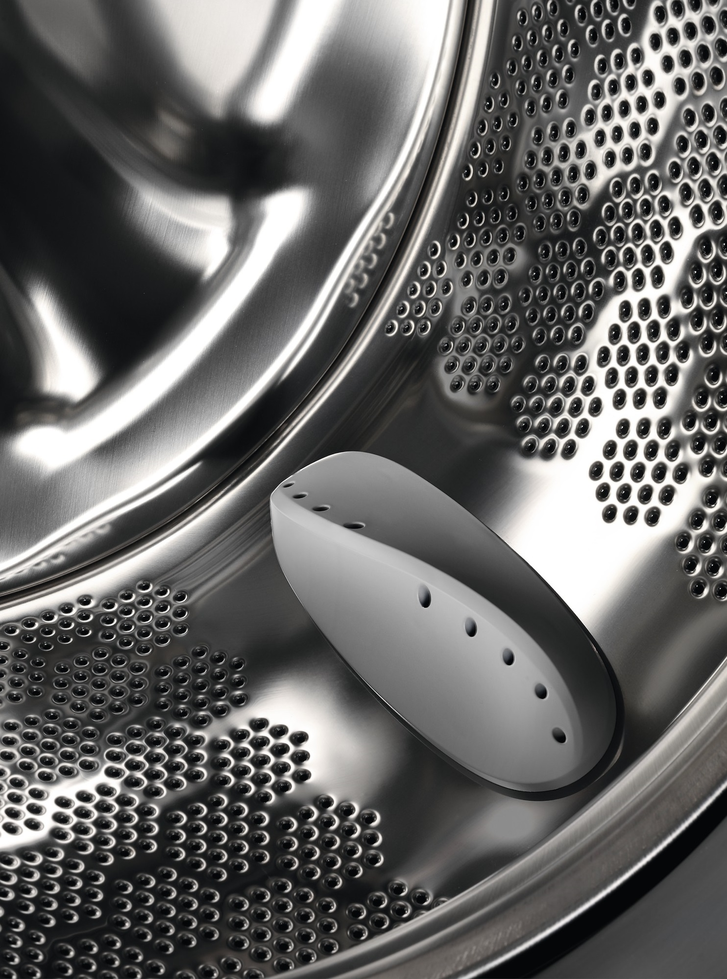 Wnętrze bębna pralki z otworami i białą plastikową częścią.